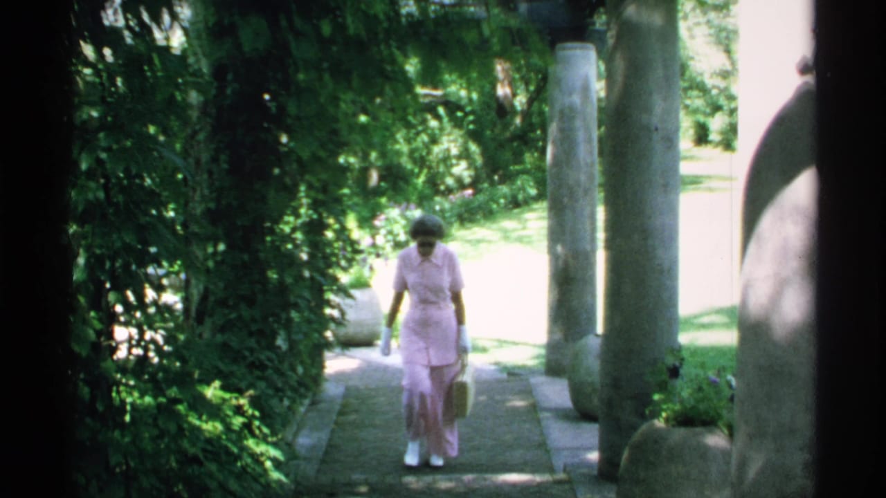 Woman in a pink outfit walks down a shaded garden path toward the camera.