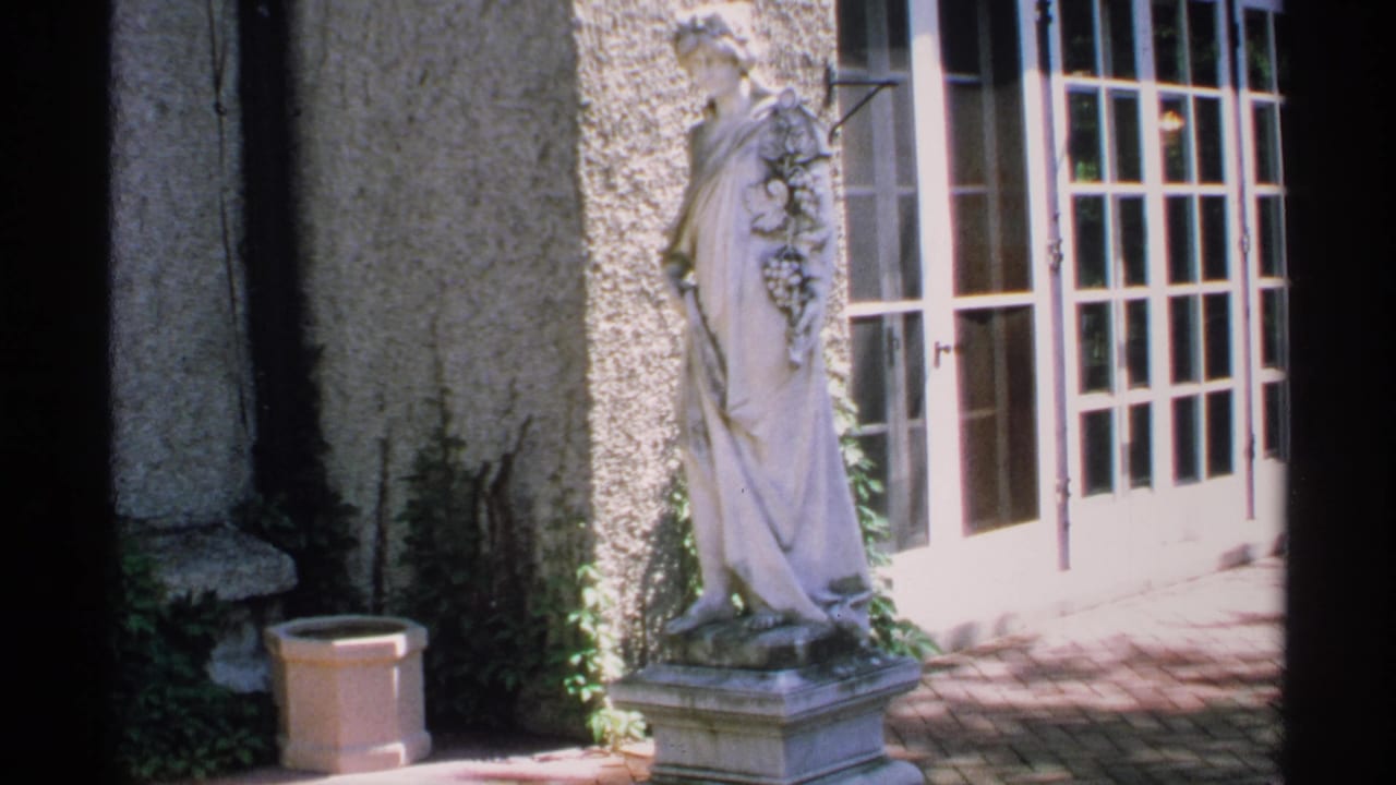 Garden statue beside stucco wall and French doors in bright sunlight.