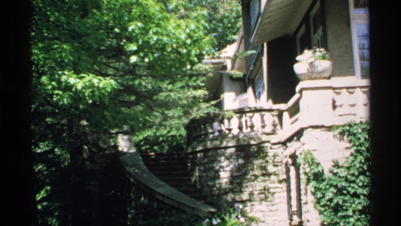 1970 Minnesota 8mm frame showing a leafy exterior view of a stone mansion with curved steps, balustrades, and white-trimmed windows.