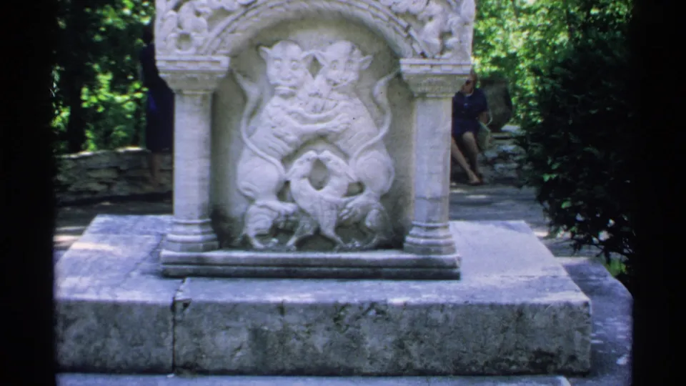 Close view of a carved stone park monument showing two lions around a bird, with a visitor partly visible in the background.