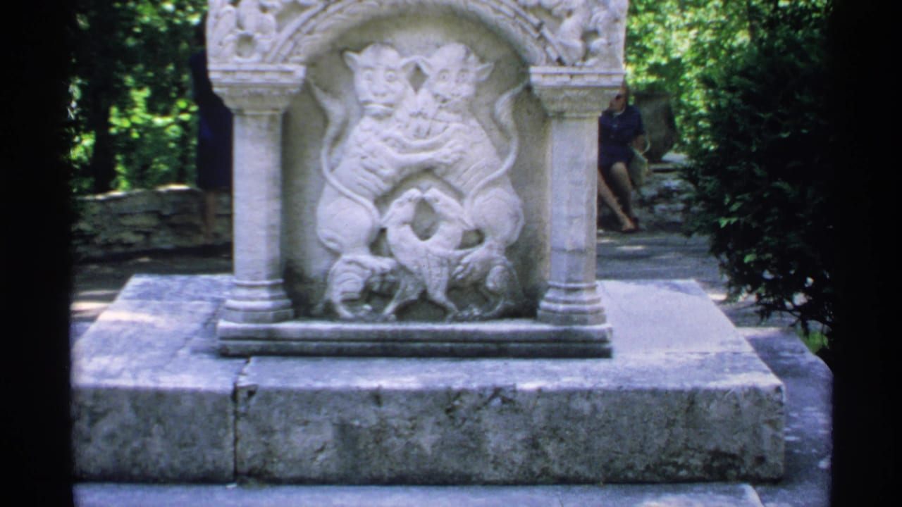 Stone relief monument with paired creatures in an arched niche, surrounded by trees.