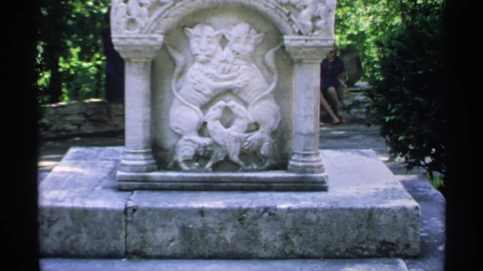 1970 Minnesota 8mm frame showing a carved stone relief monument on a low base in a wooded park setting.