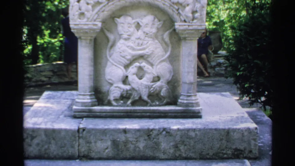 1970 Minnesota 8mm frame of a stone relief monument, with a background visitor partly visible near the path.