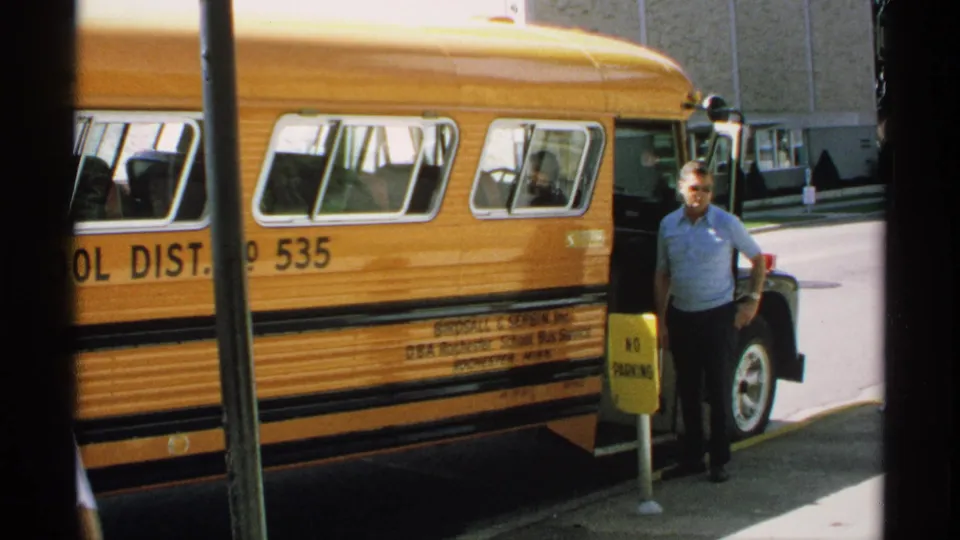1970 Minnesota 8mm frame of a yellow school bus with visible markings and an adult man by the entrance.