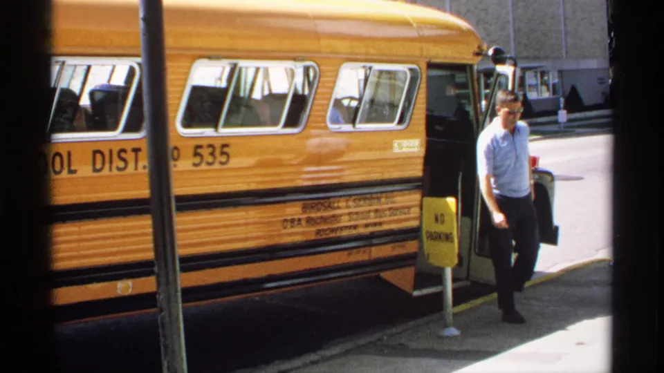 A man in a light shirt walks beside the parked yellow school bus during the 1970 Minnesota outing.