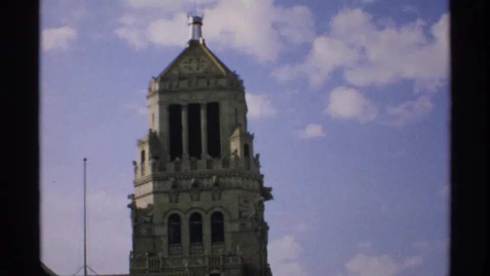1970 Minnesota home-movie frame with the tower crown centered against blue sky and soft cloud cover.