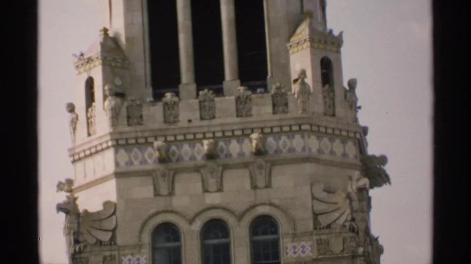 Closer 1970 Minnesota frame of the tower facade, showing arched windows, carved figures, ornament, and a small clock face.