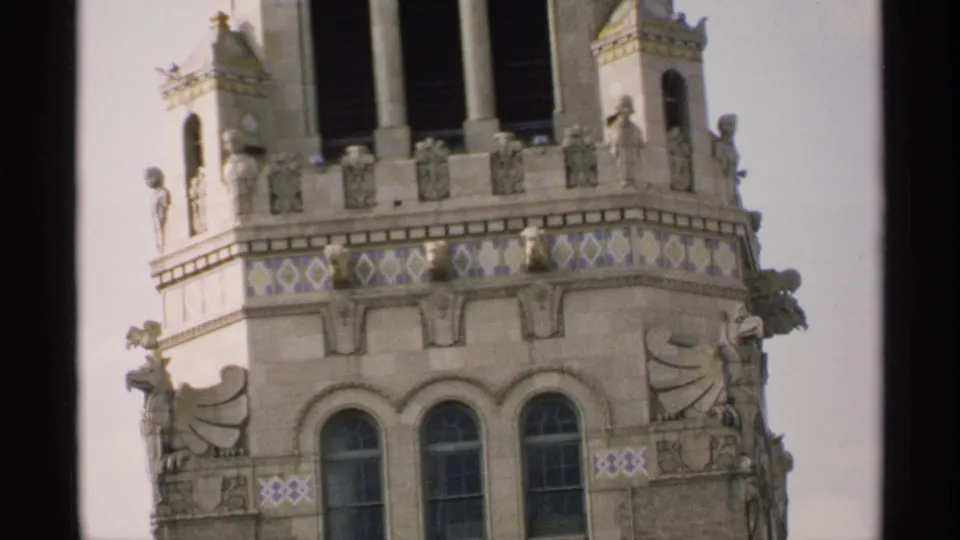 1970 Minnesota 8mm frame of a decorative building corner with arched windows, carved facade figures, and blue-yellow tile detail.