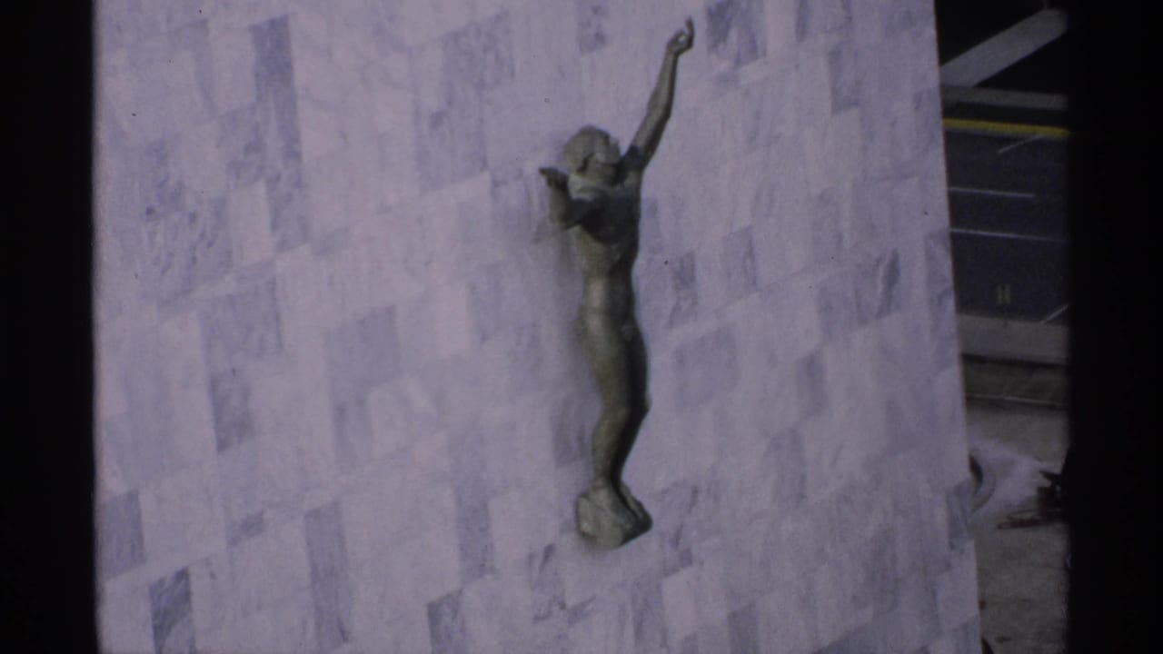 Bronze figure sculpture mounted on a pale stone building facade.