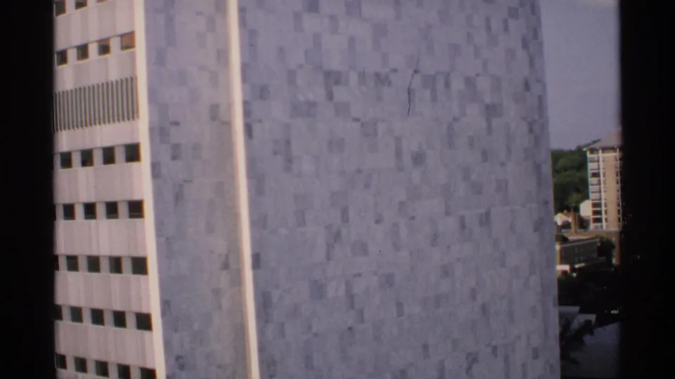 1970 Minnesota home-movie frame focused on the pale stone facade, with a vertical window band and distant buildings at the edge.