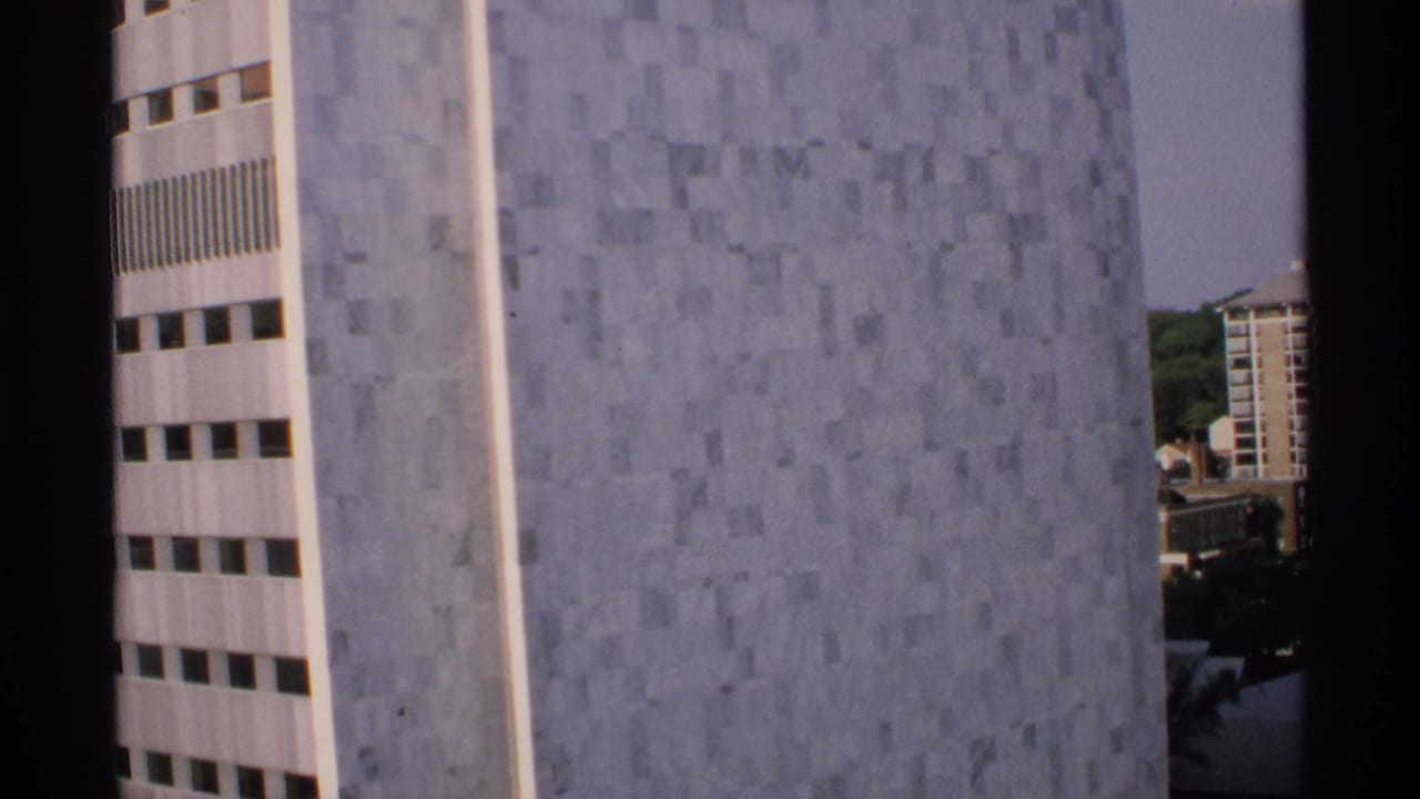 Tall building facade with gray tile panels and narrow window rows, seen through dark film borders.