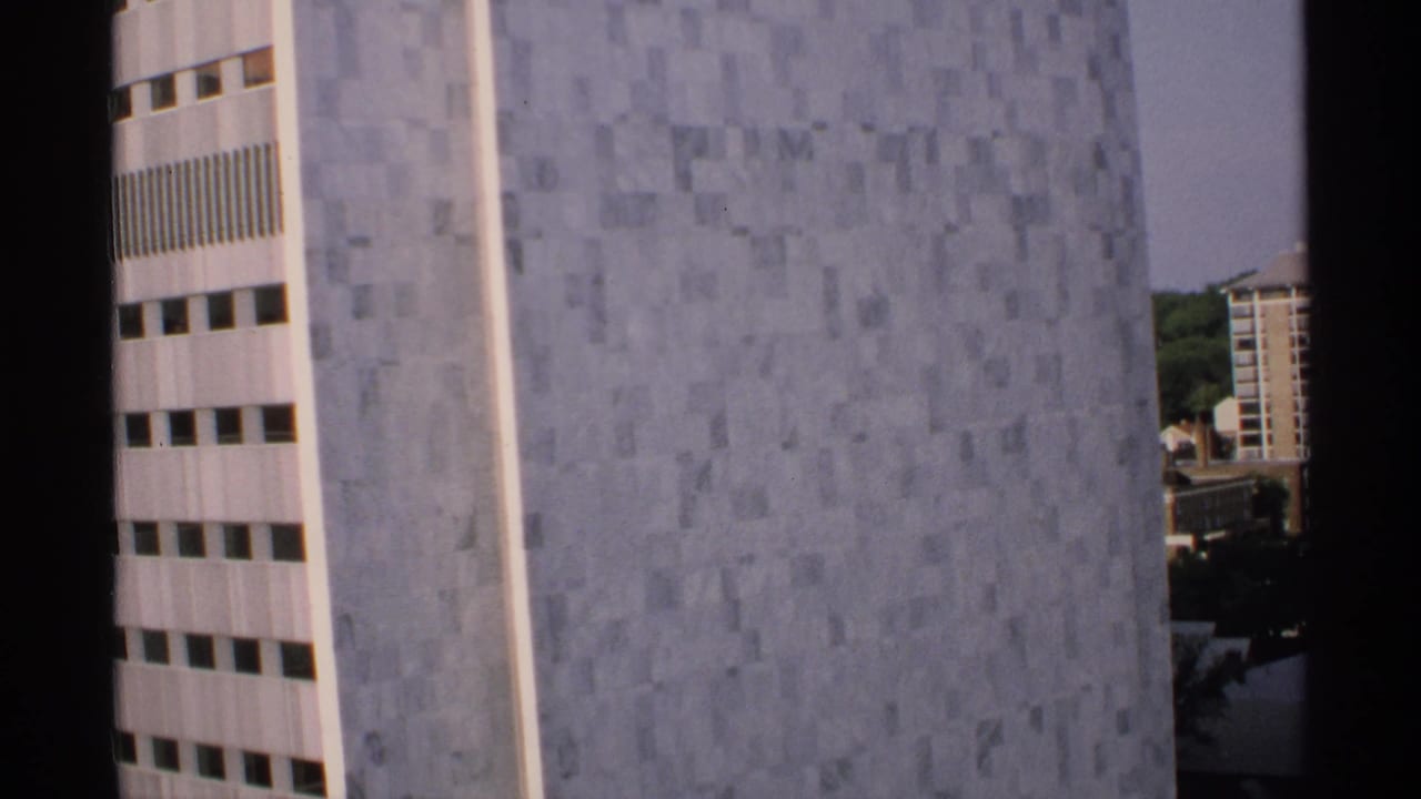 Close view of a gray tiled high-rise wall with window bands and a dark vertical border.