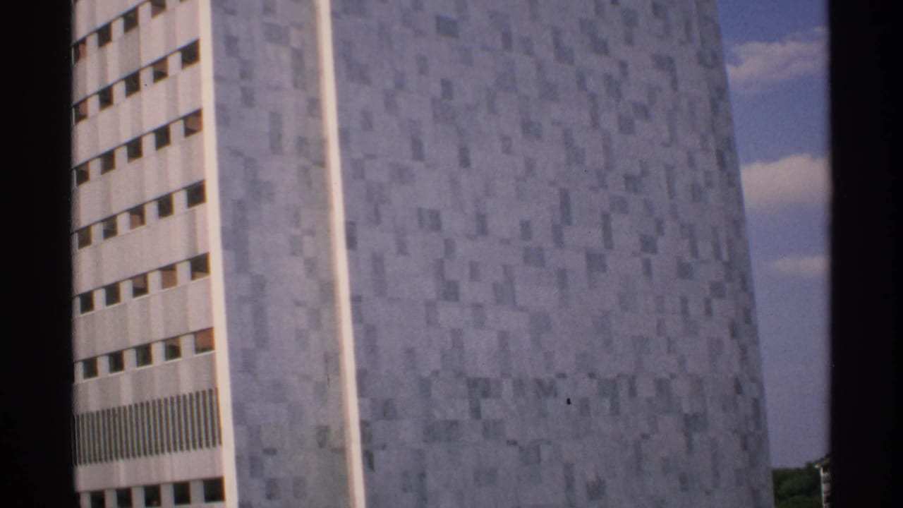 Pale modernist high-rise with narrow window rows against a blue sky.
