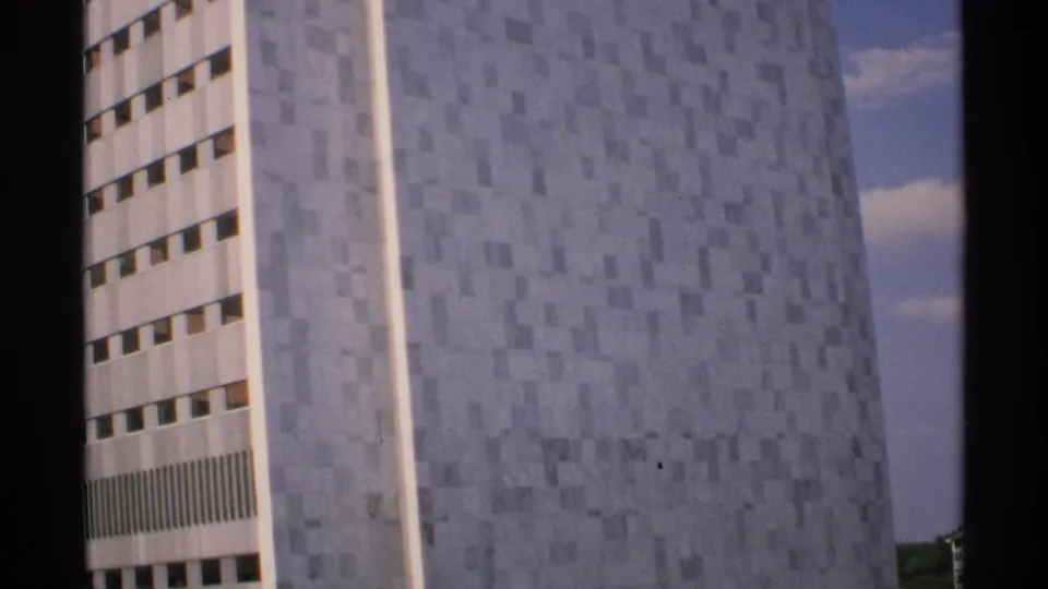 1970 Minnesota 8mm frame showing a pale patterned high-rise facade with horizontal rows of windows under a blue sky.