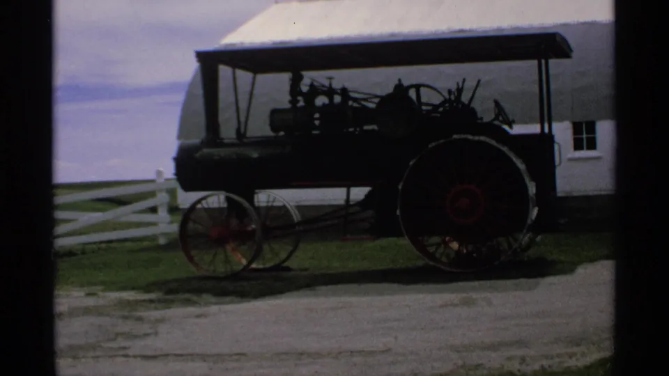 1970 Minnesota home-movie frame showing an antique vehicle exhibit near a white fence and light-colored building after the gas sign shots.