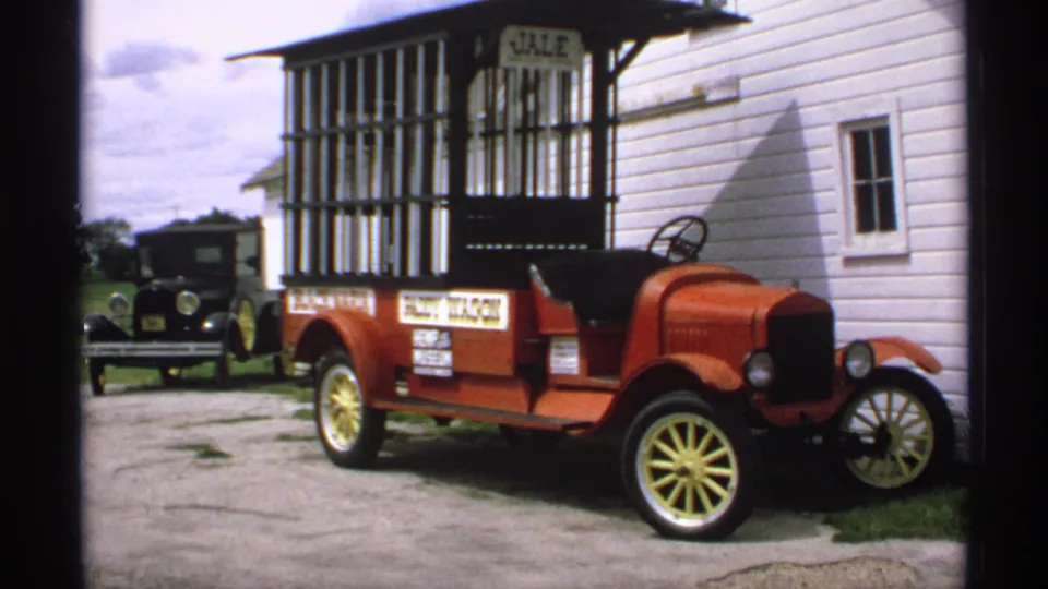Minnesota 1970 frame of the red open-top car beside the JALE-marked structure, with the black car still visible behind it.