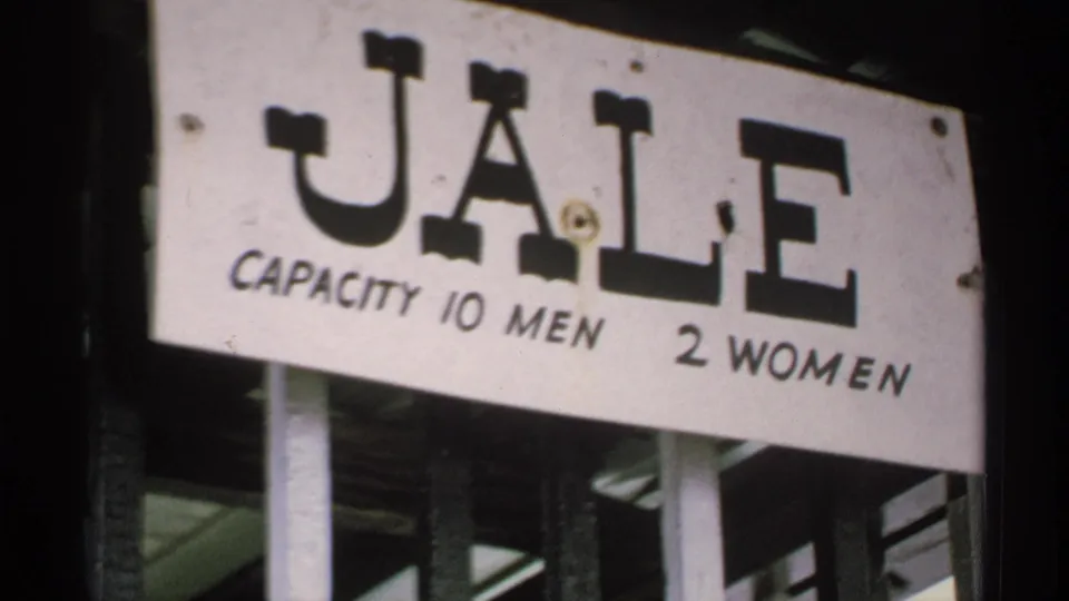 Close 8mm frame of a white sign reading JALE with capacity text for 10 men and 2 women below the large letters.