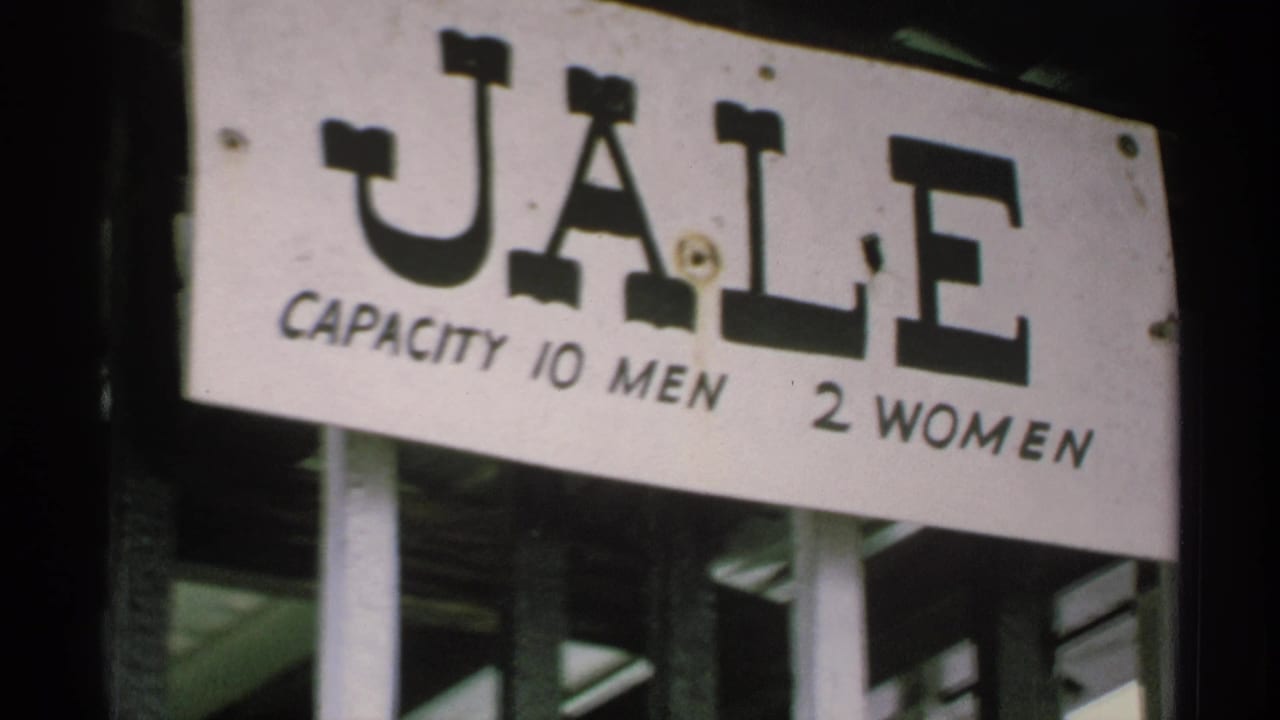 1970 Minnesota home-movie frame showing a weathered white JALE sign with capacity wording for men and women.