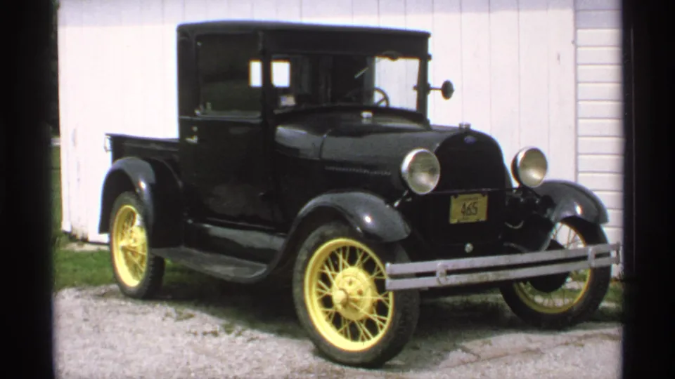 1970 Minnesota frame of the black Ford Model T pickup from a similar angle, with round lamps and yellow wheels visible.