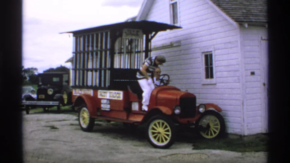 A woman in a striped shirt stands at the driver's side of the red antique paddy wagon in Minnesota, with barred sides and a JAIL sign visible.