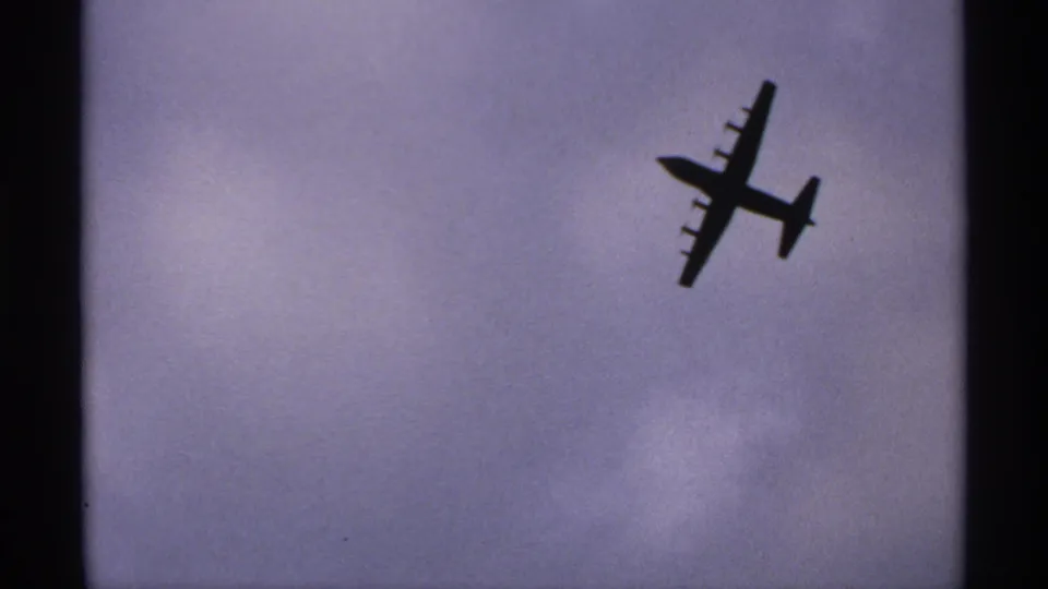 A silhouetted propeller airplane appears against a cloudy Minnesota sky in archival 8mm footage.