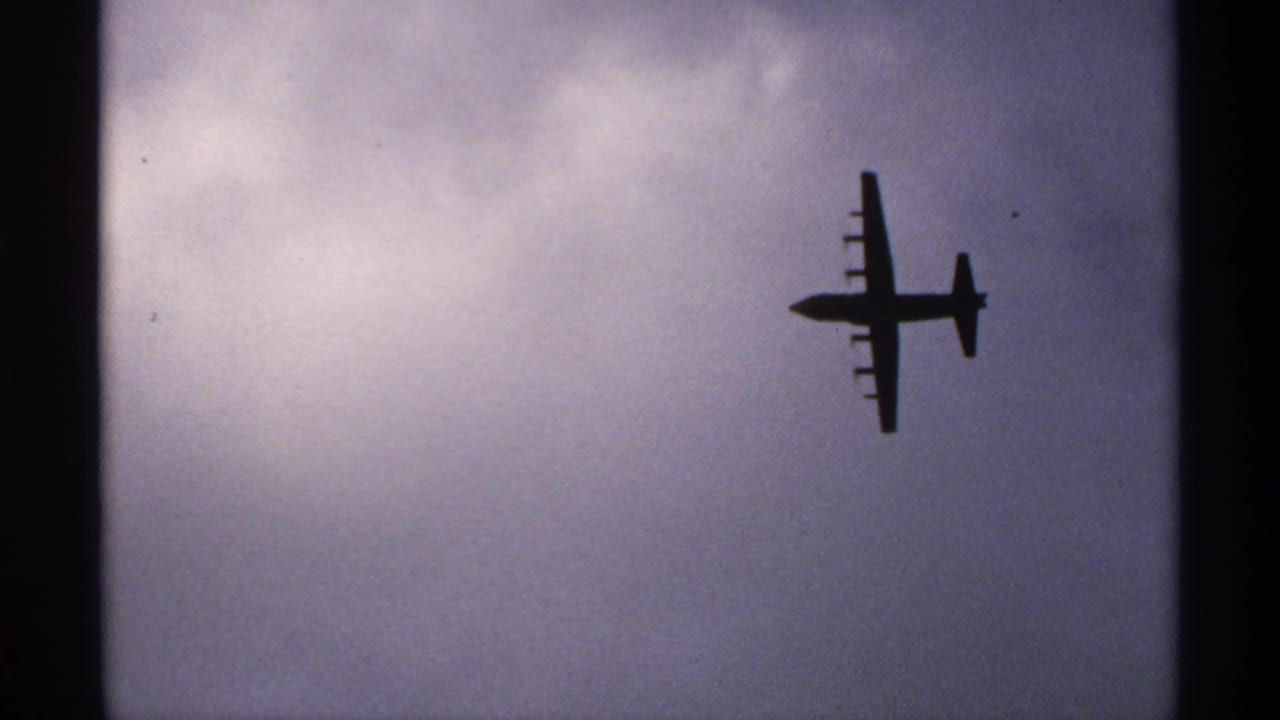 Silhouetted four-engine propeller plane against a cloudy sky.