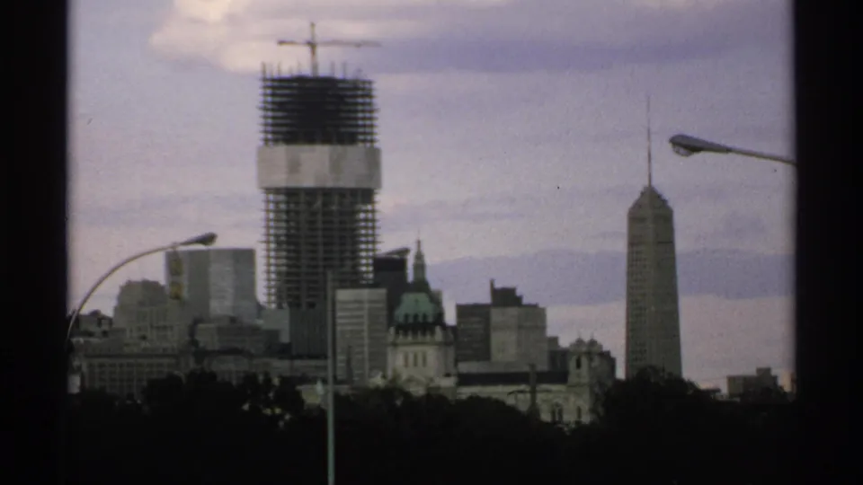 Minnesota city skyline with a high-rise under construction, crane, streetlights, and foreground trees.