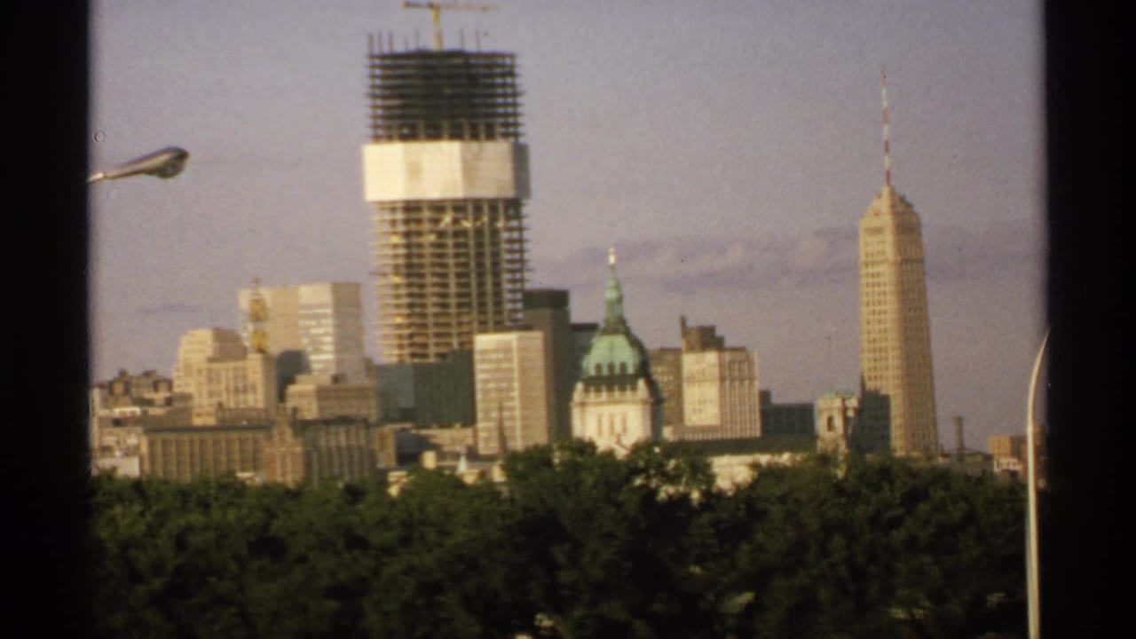 Distant Minnesota city skyline with construction tower, spired high-rise, dome, trees, and streetlight.