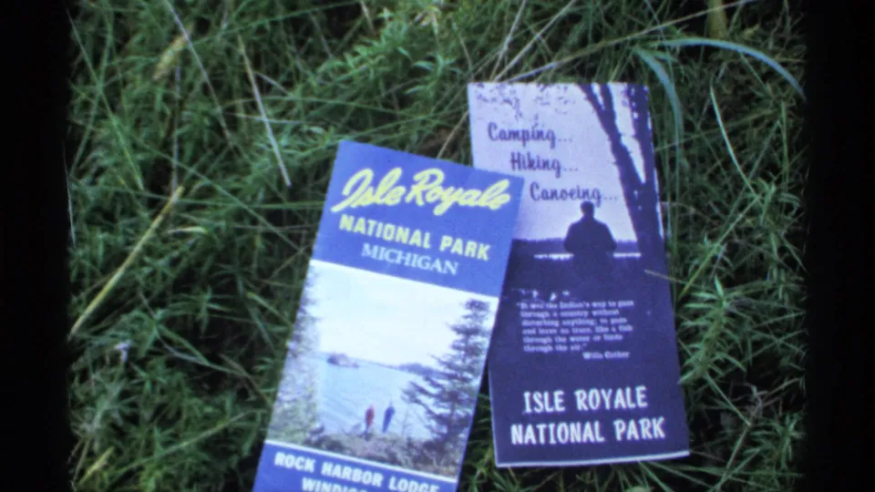 Close 8mm view of Isle Royale National Park brochures on grass, including visible park lettering and travel activity text.