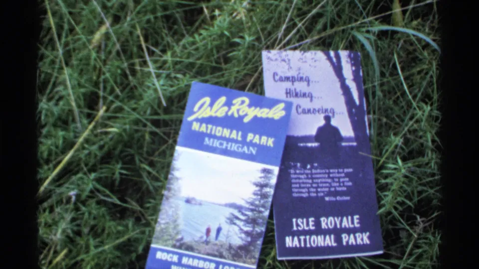 The brochures for Isle Royale National Park remain on grass, with printed recreation text and park graphics visible.