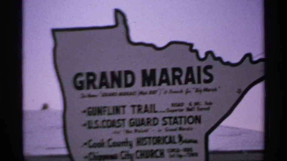 1971 8mm frame showing a Grand Marais sign near water, likely part of the Michigan road-trip sequence.