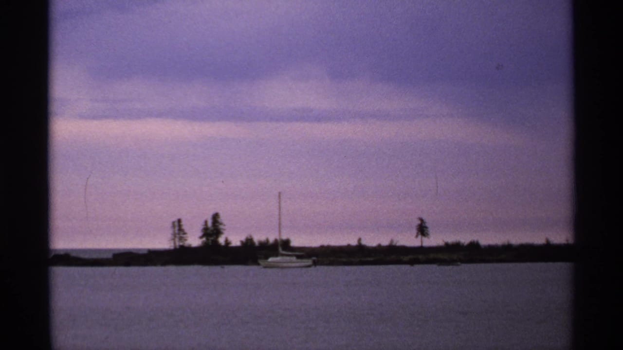 Small sailboat near a low shoreline under a purple dusk sky.