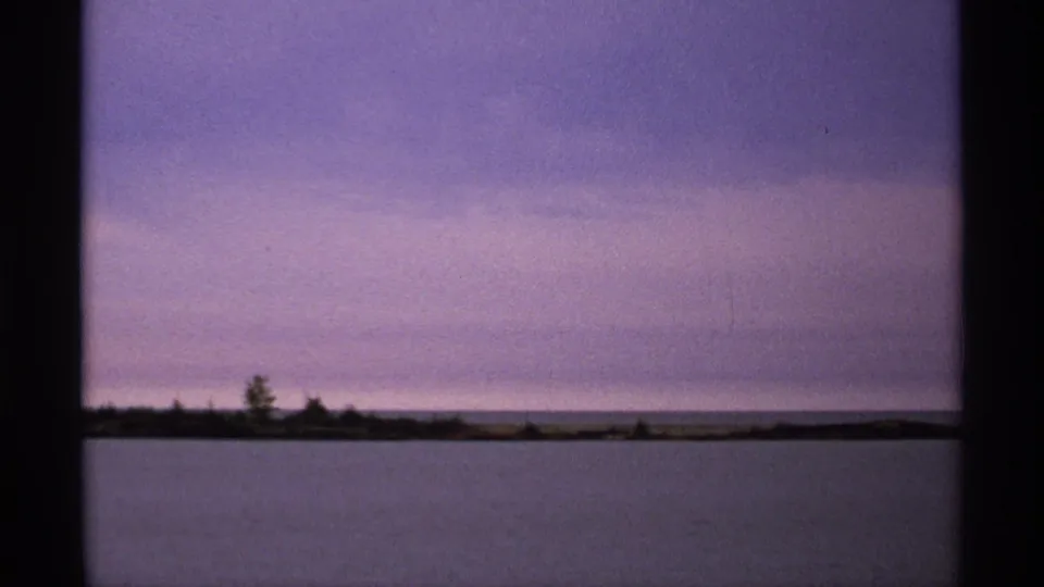 1971 8mm view of Isle Royale shoreline and calm lake water, with the boat no longer prominent in the frame.