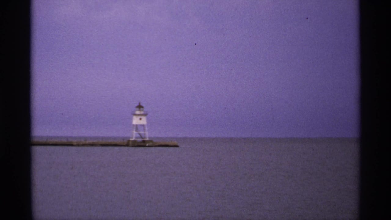 Distant white tower on a breakwater across calm water under a clear purple-blue sky.