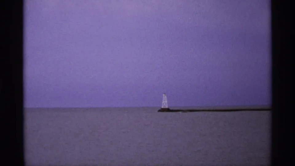 Distant Isle Royale shoreline view with a small pale tower and long breakwater under a violet-blue sky.