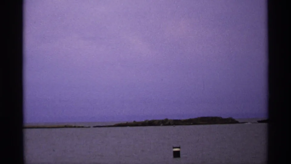 Isle Royale home-movie view of a low island across Lake Superior, with a small dark marker near the lower frame.