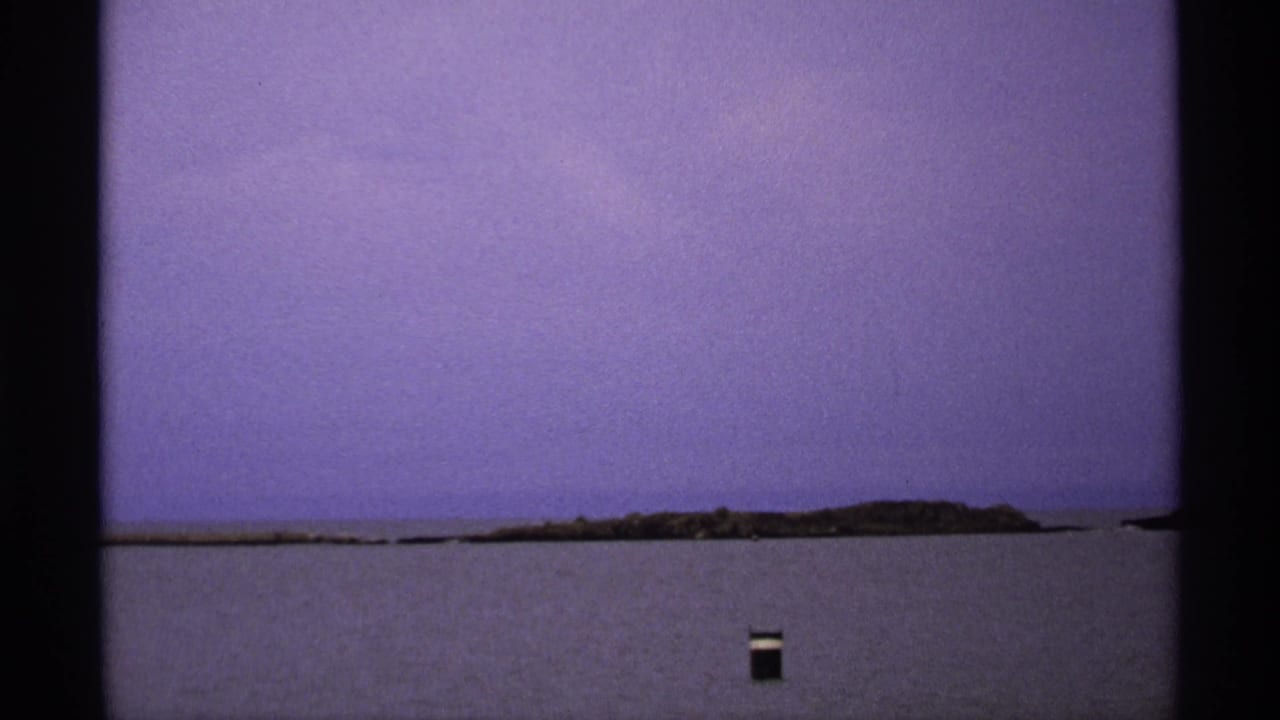 Distant low island across open water under a hazy purple sky, with a small dark floating object in front.