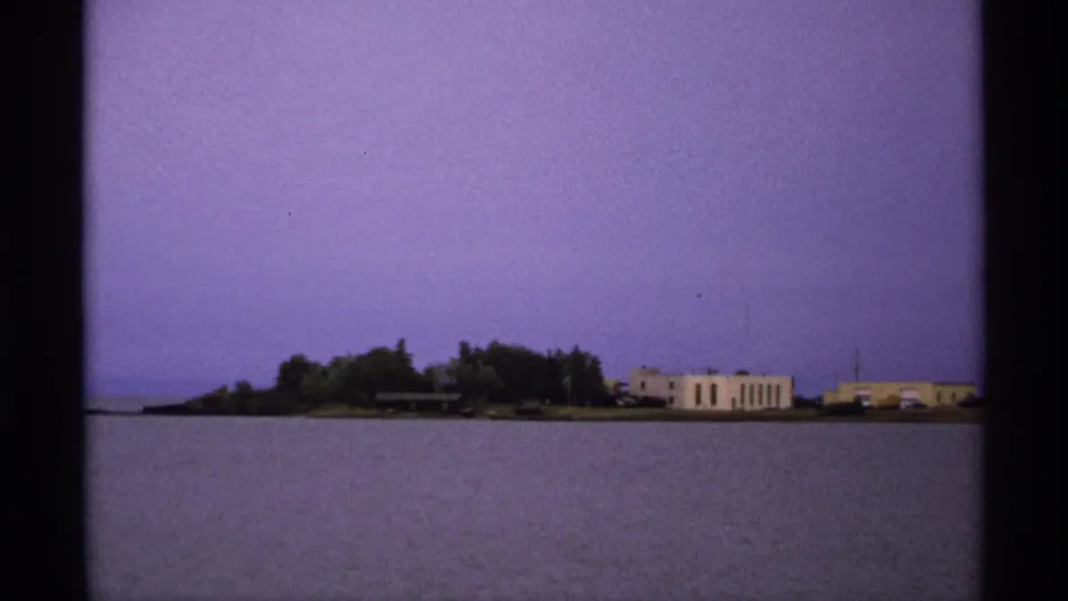 1971 Isle Royale view with trees and pale shoreline buildings appearing across the water in grainy 8mm footage.