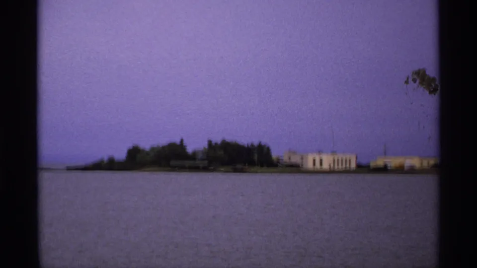 Isle Royale shoreline in 1971 with trees, pale buildings, and open water captured from a visitor-like viewpoint.