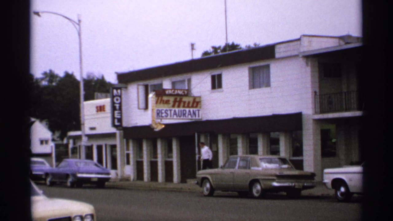 1971 8mm street view in Isle Royale, Michigan, showing The Hub Restaurant and motel, parked cars, and a man near the storefront.