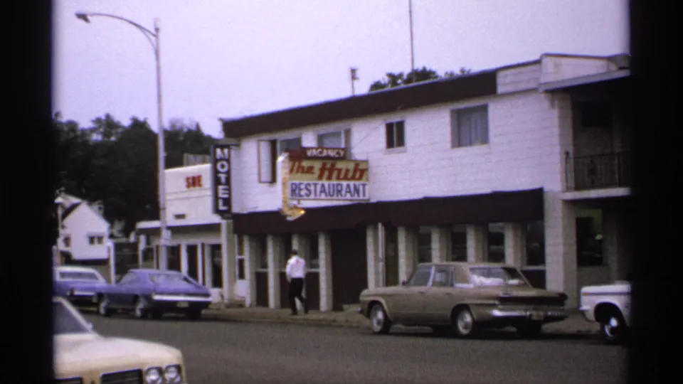A 1971 Isle Royale street scene shows a man walking past The Hub Restaurant and Motel, with period cars parked at the curb.