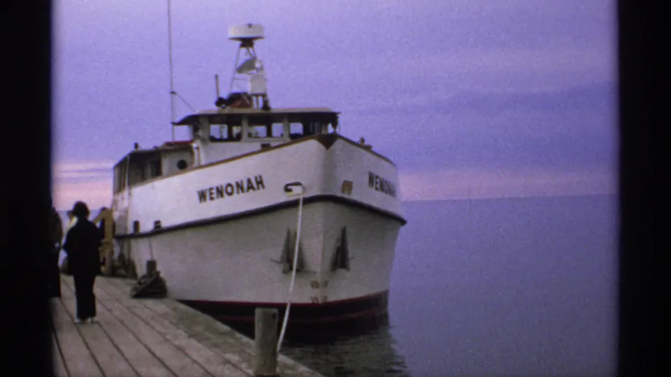 1971 Isle Royale home-movie frame of the WENONAH at dock, with a person on the pier and hazy open water in the background.