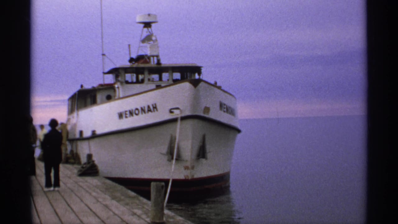 White Wenonah boat docked beside a wooden pier with silhouetted passengers nearby.