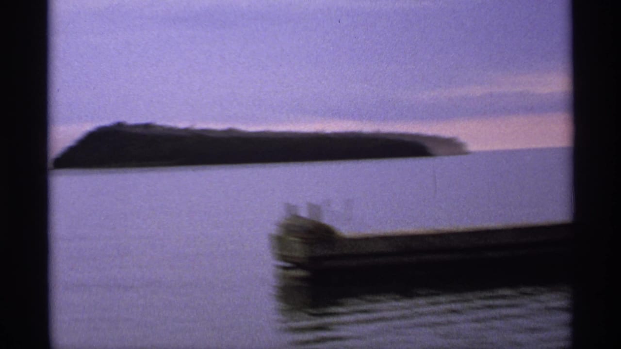 Calm lake with a dark wooded island and a blurred boat or dock in the foreground.