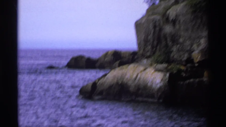 Handheld 8mm frame of Isle Royale rock formations and blue lake water, with soft focus and faded color typical of home-movie film.