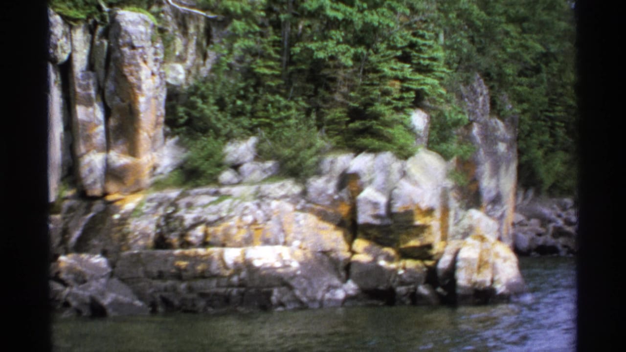 Rocky shoreline with evergreen trees above calm lake water.