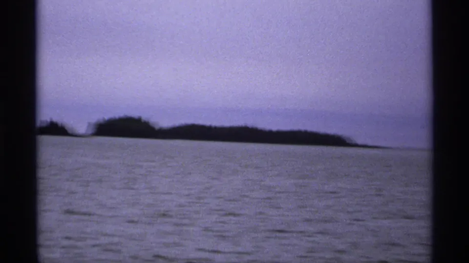1971 Isle Royale 8mm frame with dark forested island shapes across the lake under a soft overcast sky.