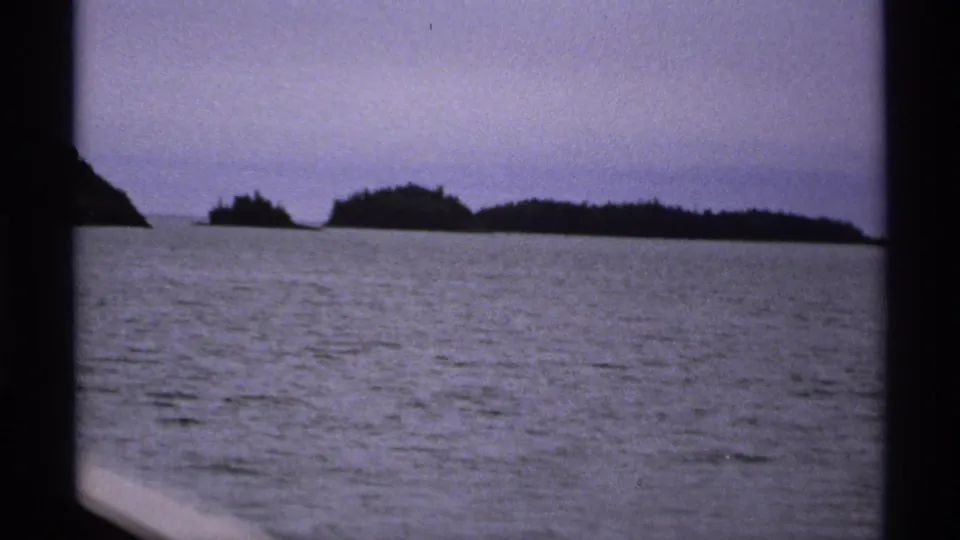 1971 Isle Royale 8mm frame showing open water, distant wooded island shapes, and dark film-gate borders from a handheld boat view.