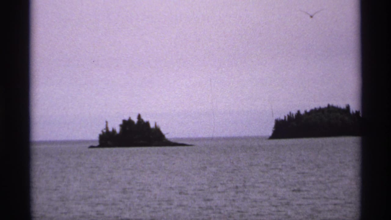 Two small forested islands across calm lake water under a purple sky.