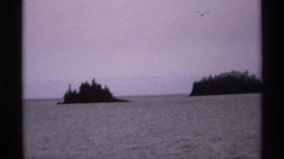 1971 Isle Royale frame with wooded islands across the lake and a faint bird-like shape above the purple horizon.
